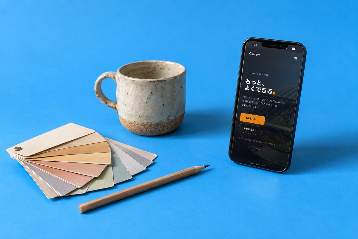会社サイトを表示したスマートフォンと色見本・マグカップ（Quickry Web制作のイメージ）